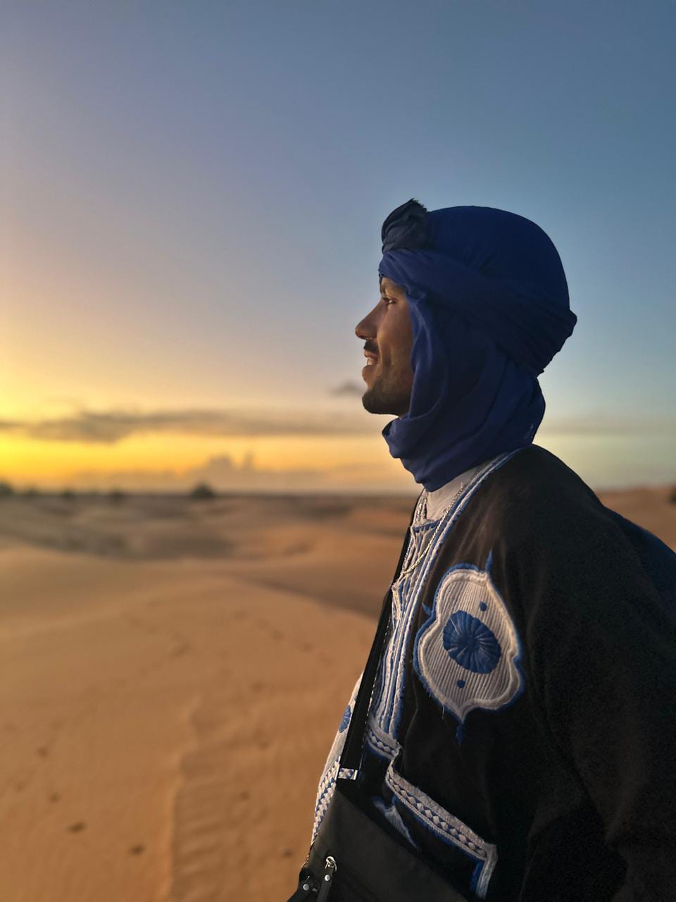 Sunset over the Sahara dunes in traditional blue attire