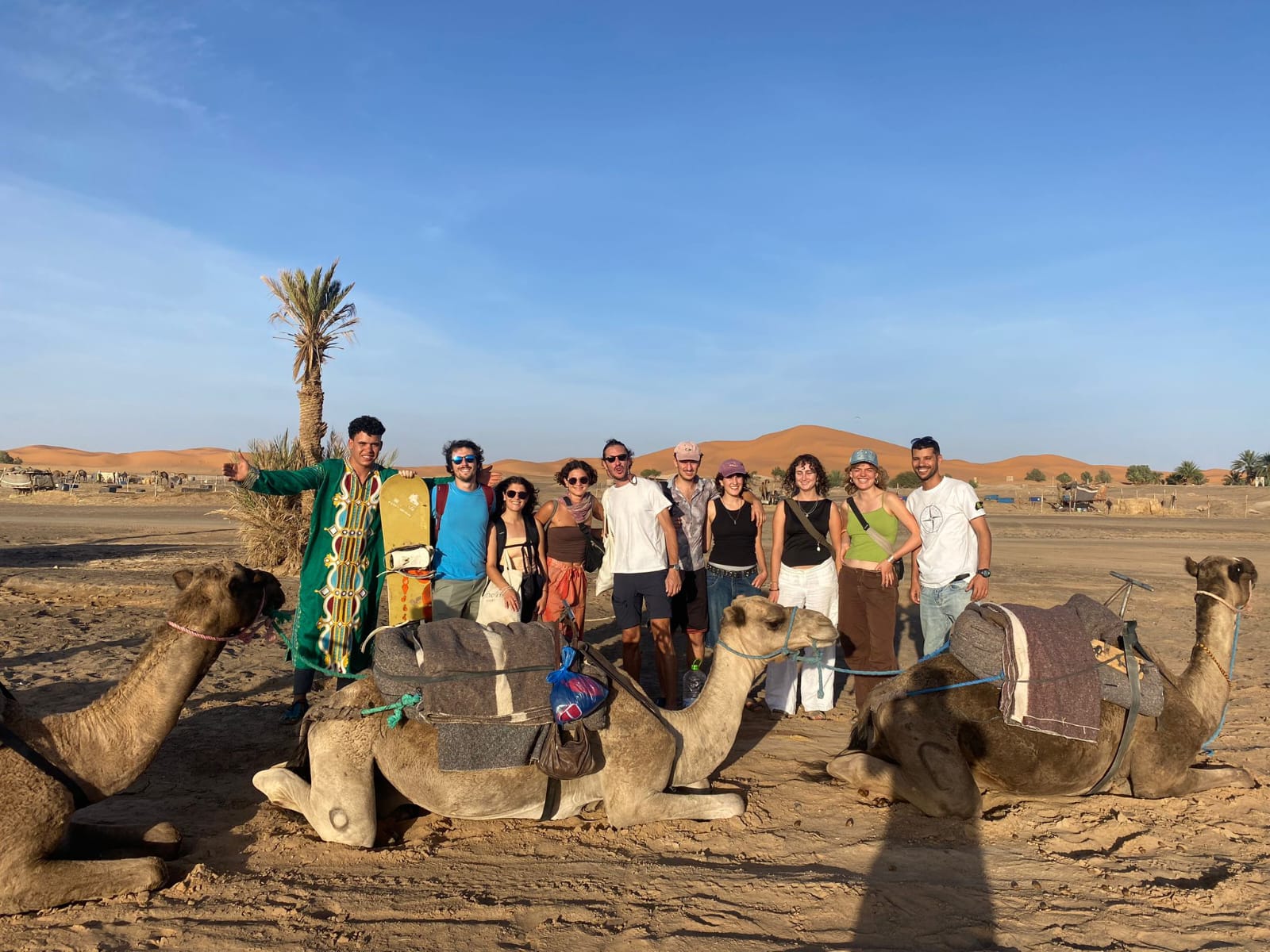 Happy travellers with camels and their local guide in the Sahara dunes